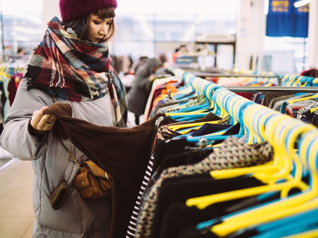 Young woman is browsing a rail of clothes at mall store